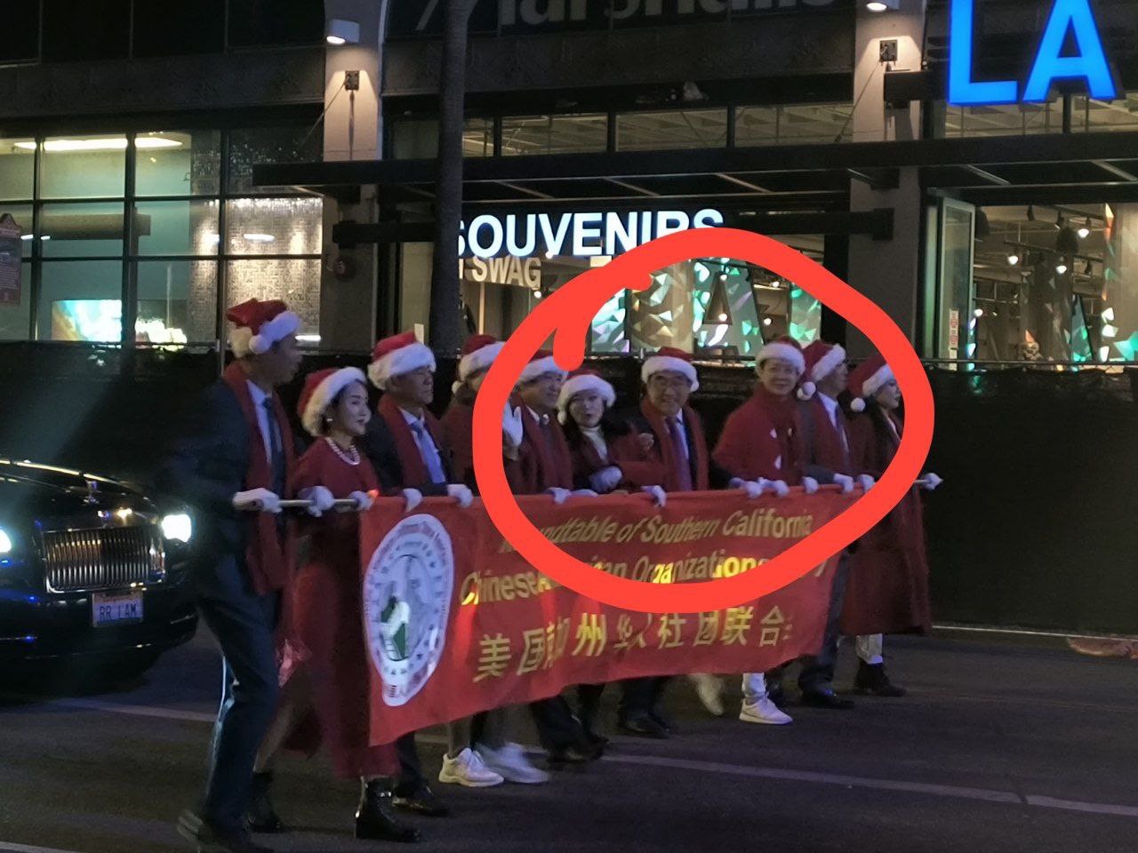 中國民主黨成員和民主人士數十人參加了遊行,和平抗議自己被洛杉磯中領館及親北京的“美國華人社團聯合會”所代表。紅圈中戴眼鏡者為洛杉磯中領館縂領事郭少春。(圖片來源：界立建）